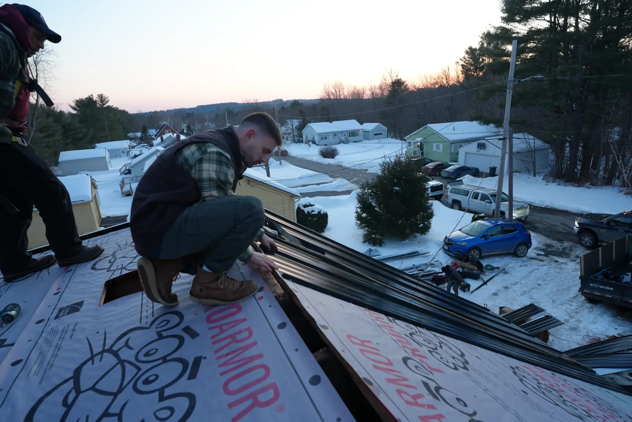 GraniteShield Roofing owner installing standing seam metal roofing panels during a Maine winter project at dusk