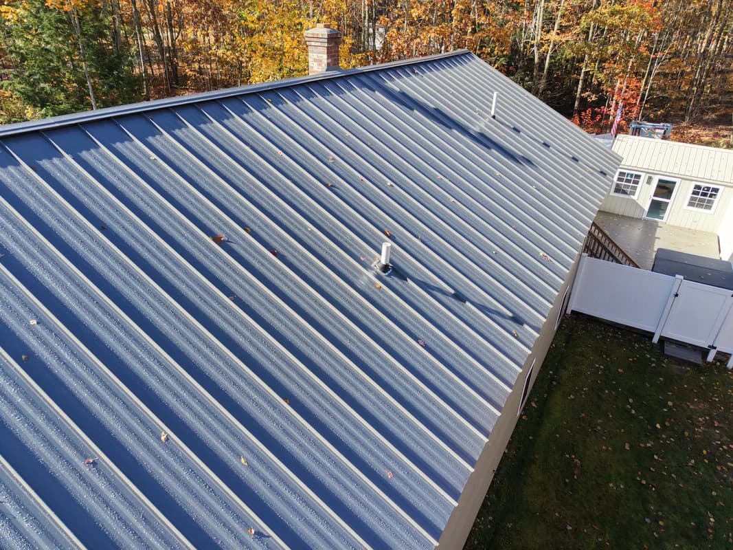 Blue standing seam metal roof on residential home in Maine - aerial drone view with fall foliage