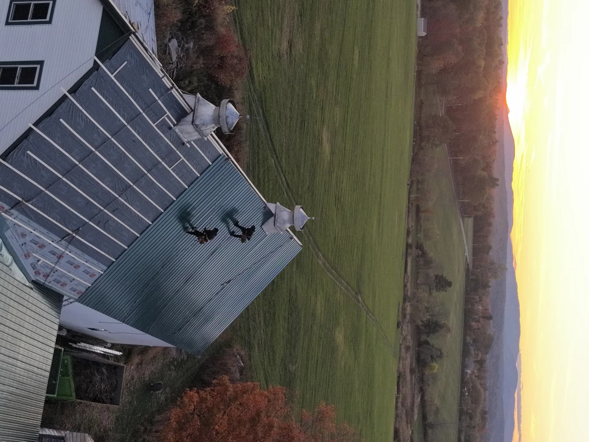 Standing seam metal roof installation on Maine barn at sunset - professional metal roofing with cupolas