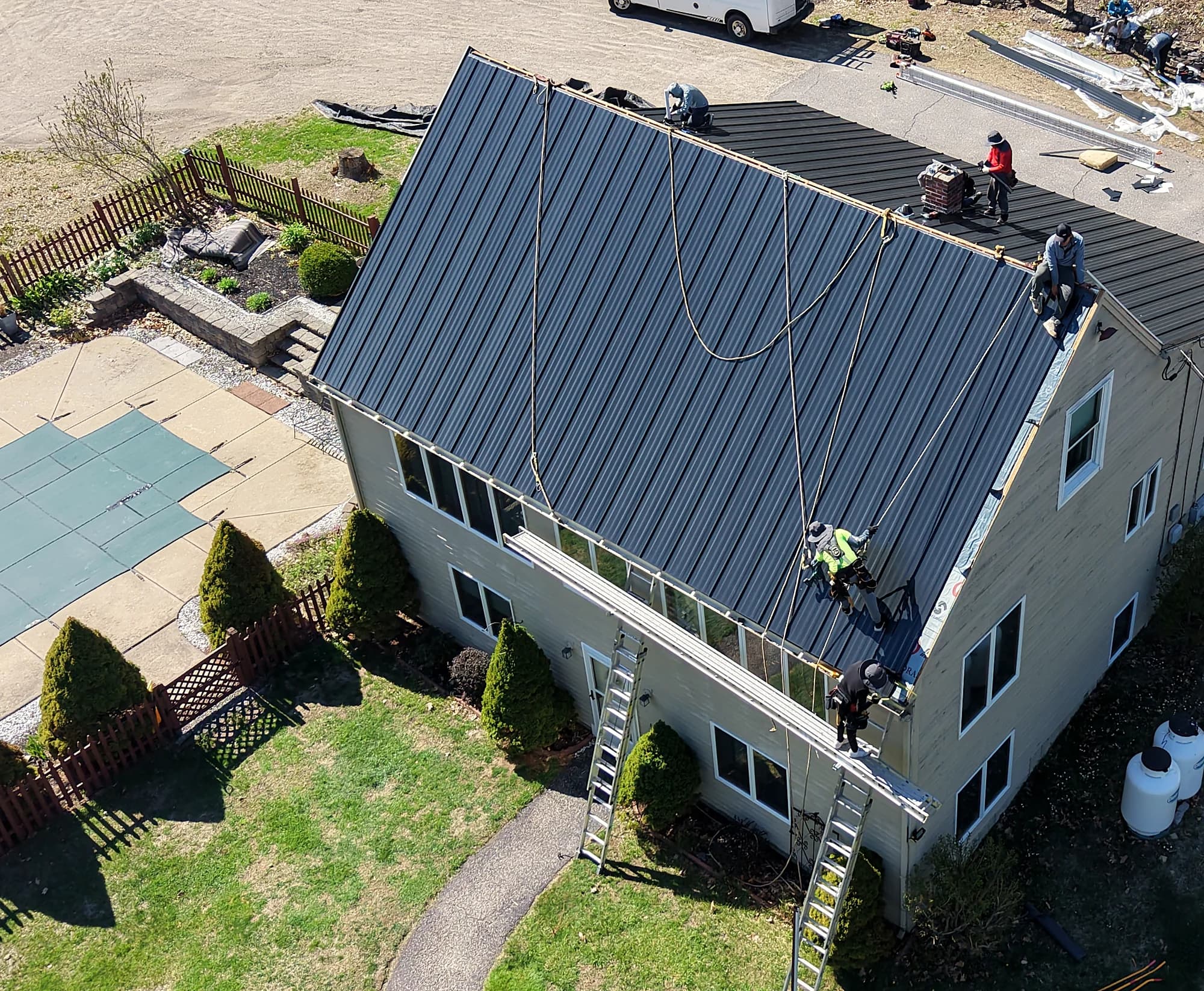 Crew installing a matte black standing seam metal roof on a home in Gorham, Maine by GraniteShield Roofing & Exteriors